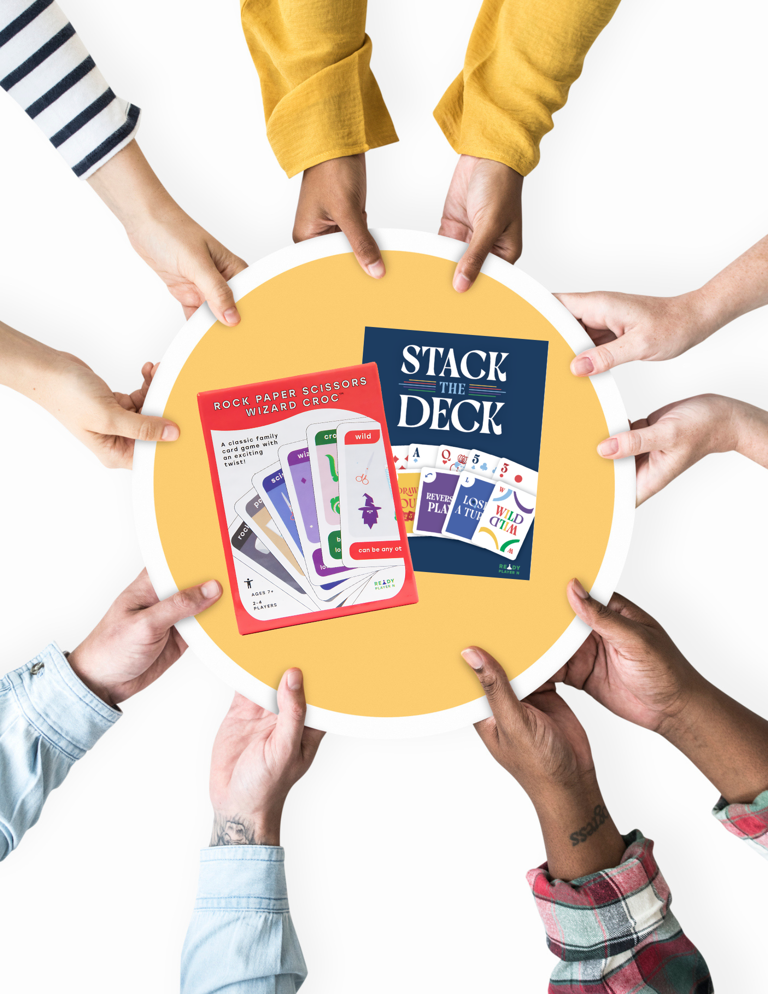 Hands reaching towards a yellow plate with 'Rock Paper Scissors Wizard Croc' and 'Stack the Deck' card game packaging in the middle